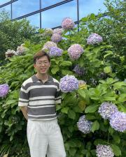 Yuan-Hsi Chao standing in front of a bush with large purple flowers